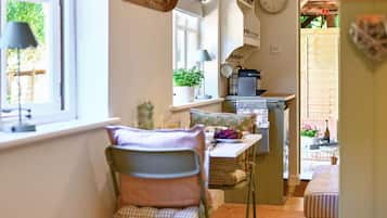 Une cuisine chaleureuse avec un coin repas, une horloge au mur et une fenêtre donnant sur un paysage verdoyant.