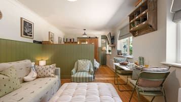 A cozy room with a green upholstered sofa, a striped armchair, a dining table with chairs, and a wooden shelf with various items.