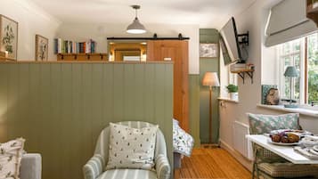 A cozy room with a striped armchair, a dining table with a plate of fruit, a lamp, and a bookshelf.