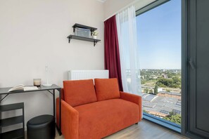 Una sala de estar moderna con un sofá, una mesita con una lámpara, un radiador y vistas a un paisaje urbano a través de un ventanal grande.