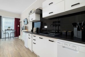 A modern kitchen with white cabinetry, a black countertop, and a built-in dishwasher. - Funkcjonalne Studio z Klimatyzacja i Miejscem do Pracy by Noclegi Renters (Katowice)