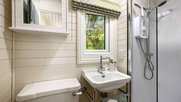 A bathroom with a white sink, a toilet, a window with a polka dot valance, and a shower area.