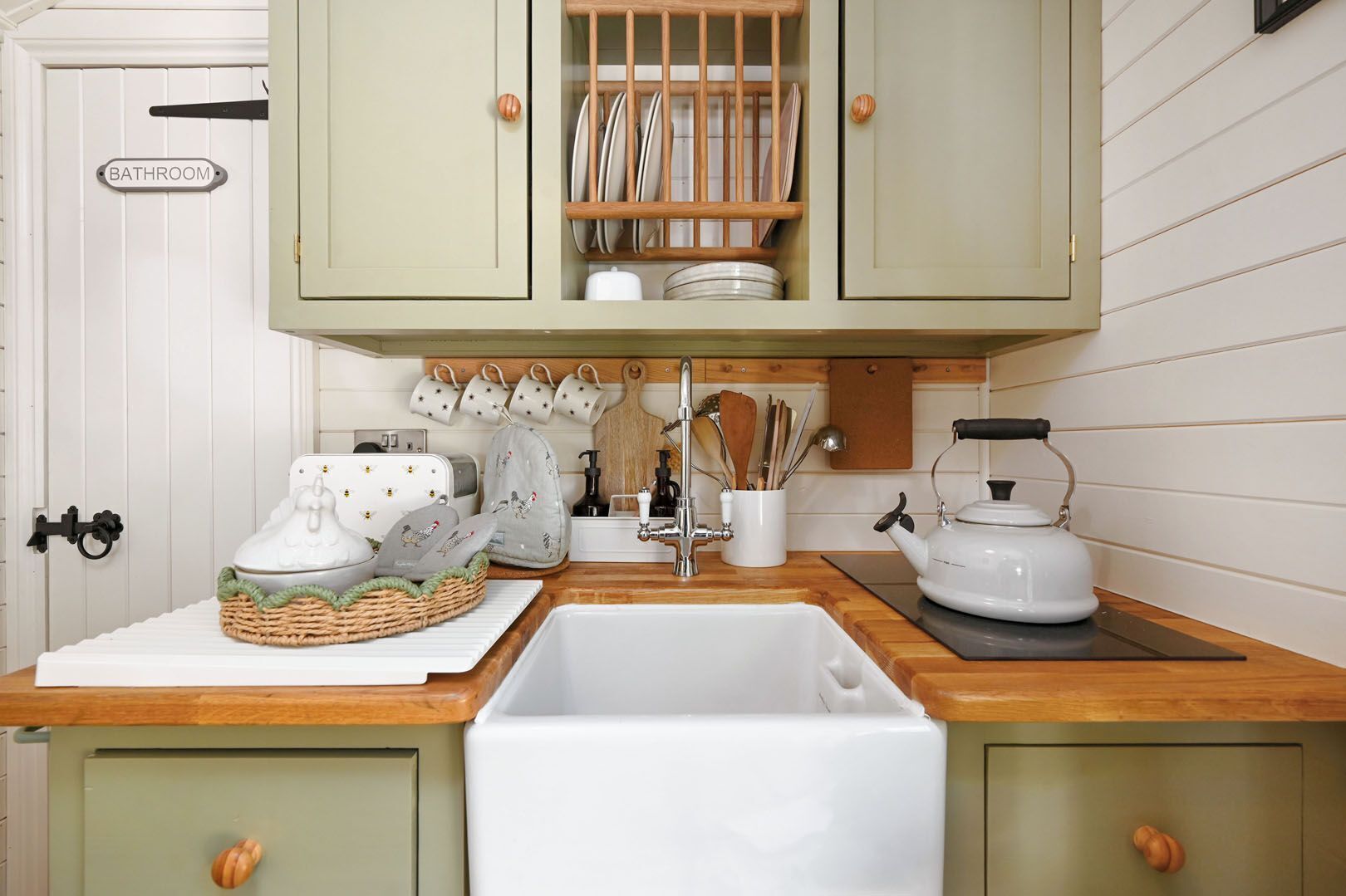 A kitchen with a sink, a kettle, and a cabinet with dishes.