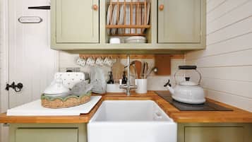A kitchen with a sink, a kettle, and a cabinet with dishes.