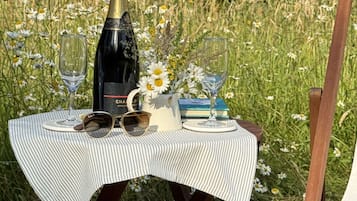 A picnic setup with a bottle, glasses, and a book on a table in a grassy area.