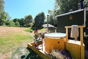 A hot tub with a wooden deck, surrounded by a garden with flowers and a wooden fence.