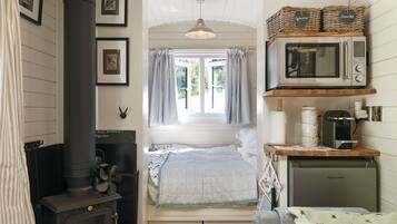 A compact bedroom with a bed, a window with curtains, a stove, and a kitchenette with a microwave and kettle.