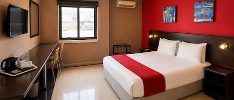 A hotel room with a bed, bedside tables, a desk with a chair, a television, and artwork on the walls.