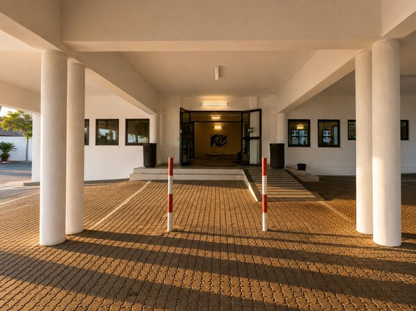 A covered walkway with a patterned floor, white pillars, and a glass door entrance.