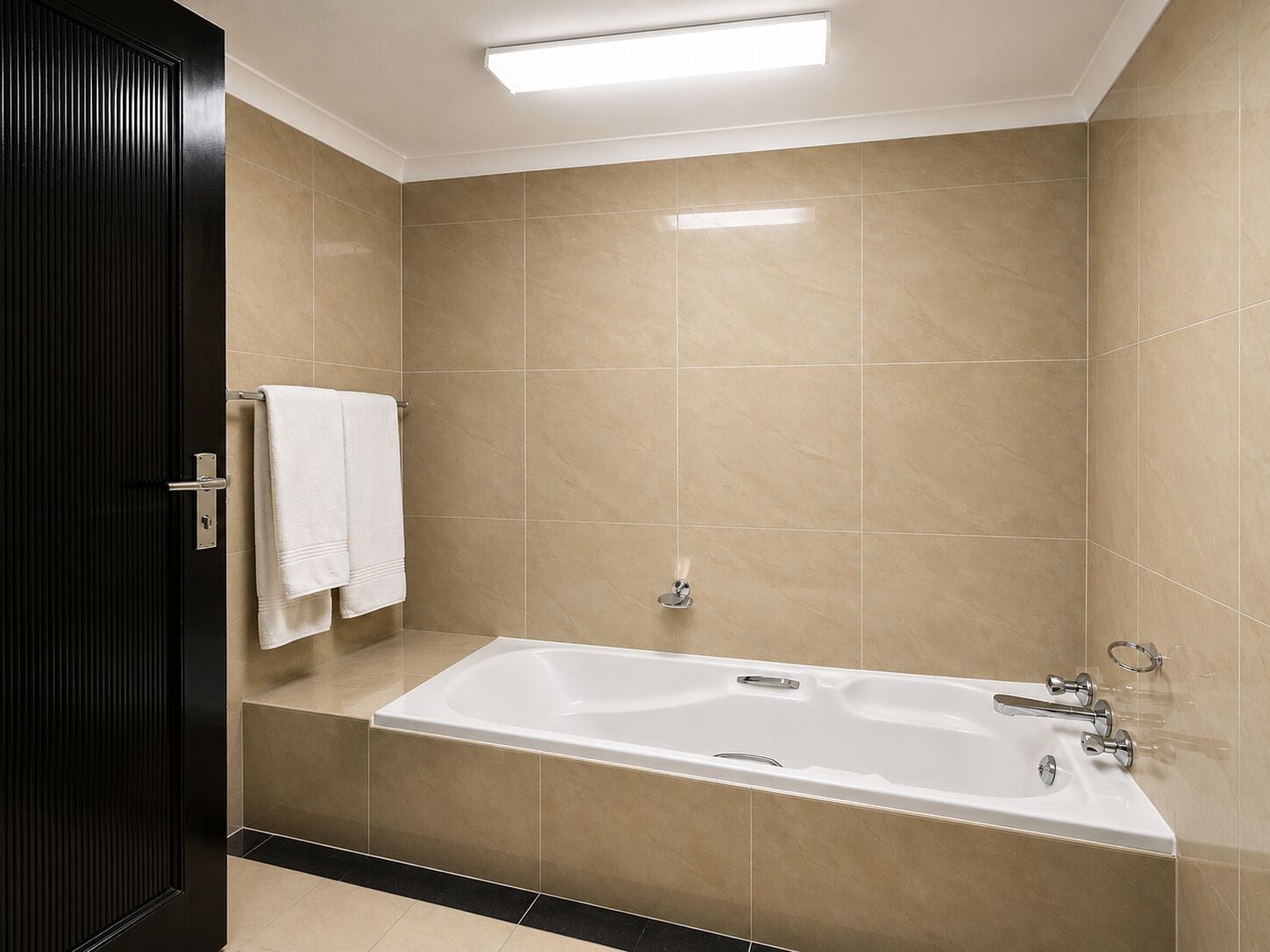 Ein modernes Badezimmer mit einer Badewanne, beigen Fliesen und einem Handtuchhalter.