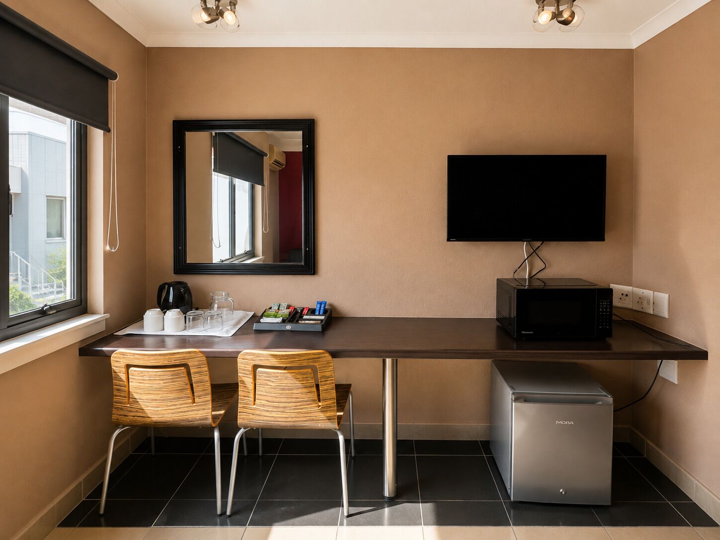 Quarto de hotel compacto com escrivaninha, duas cadeiras, televisão, micro-ondas e frigorífico.