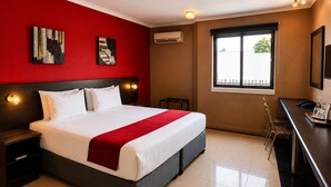 A hotel room with a large bed, a desk, a chair, and artwork on the walls.