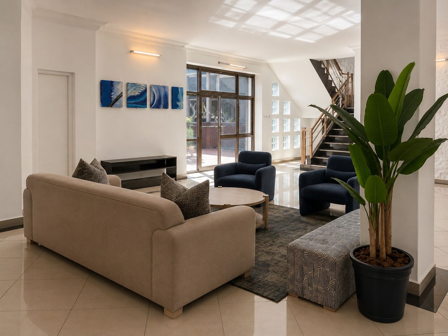A modern living room with a beige sofa, two armchairs, a coffee table, and a large potted plant.