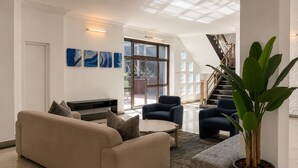 A modern living room with a beige sofa, two armchairs, a coffee table, and a large potted plant.