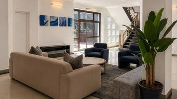 A modern living room with a beige sofa, two armchairs, a coffee table, and a large potted plant.