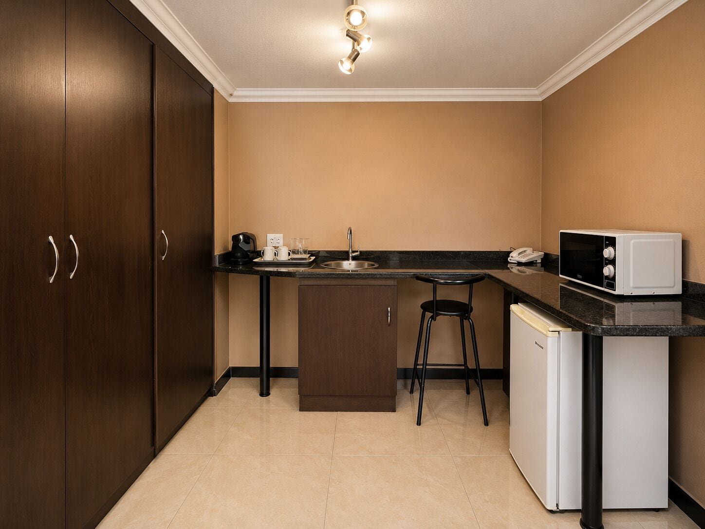 Uma cozinha compacta com pia, micro-ondas e cafeteira.
