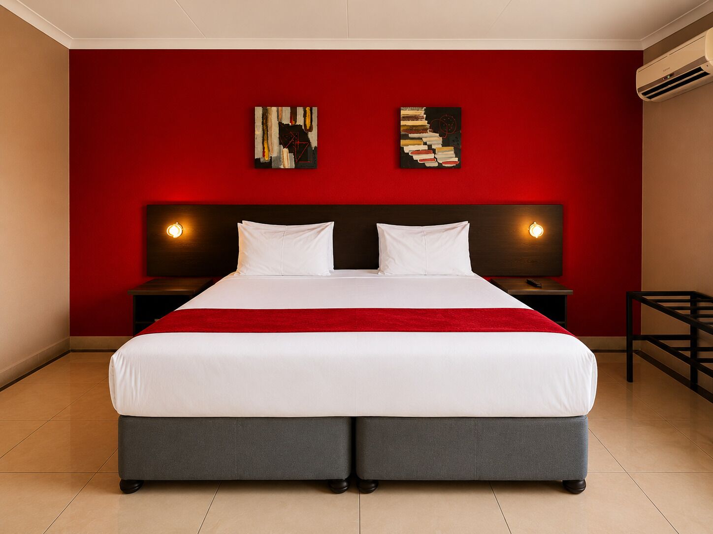 A double bed with a red accent wall, two bedside tables with lamps, and abstract artwork on the wall.
