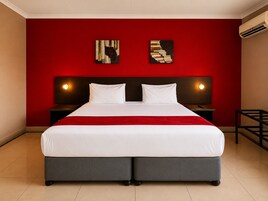 A double bed with a red accent wall, two bedside tables with lamps, and abstract artwork on the wall.