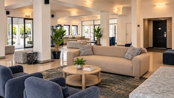 Un hall d’entrée spacieux, avec un canapé beige, des fauteuils bleus et une table basse ronde.