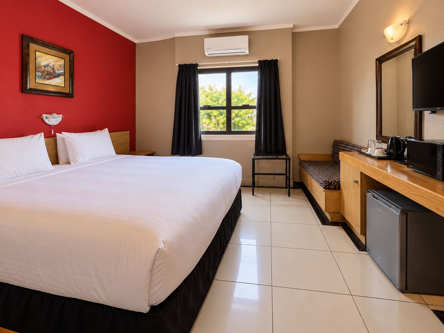 Una habitación de hotel con una cama, un escritorio con microondas, televisión y ventana con cortinas.