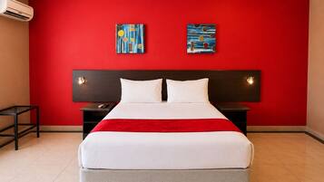 Habitación de hotel con pared roja, una cama grande con ropa blanca, dos mesitas de noche y una obra de arte sobre la cama.