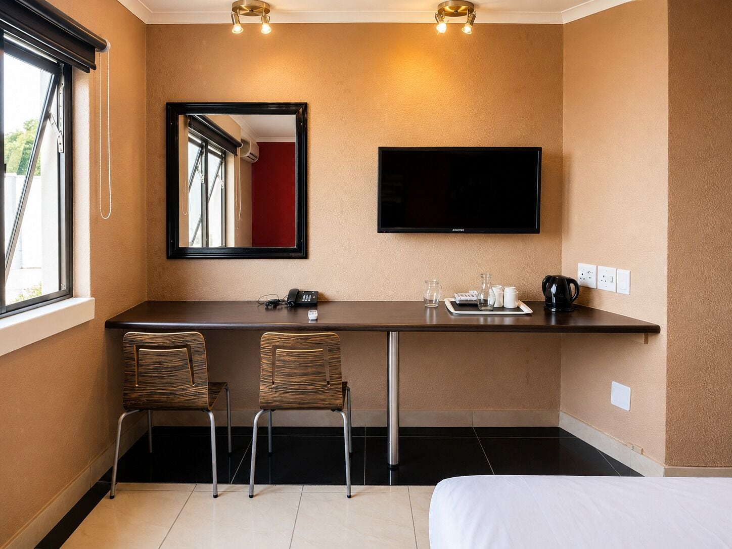 Habitación de hotel con cama, escritorio con dos sillas, televisor de pantalla plana y espejo.