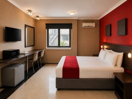 Habitación de hotel con cama, escritorio, silla, televisión, aire acondicionado y obras de arte en las paredes.