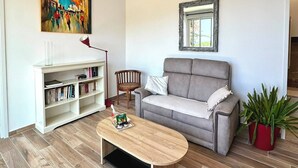 A living room with a grey sofa, a wooden coffee table, a bookshelf, a painting, and a potted plant. - One-bedroom apartment in Rupione with exceptional ocean views, a 6-minute walk from the beach (Pietrosella)