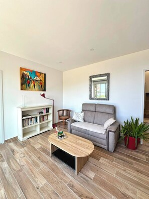 A living room with a grey sofa, a wooden coffee table, a bookshelf, a painting, and a potted plant. - One-bedroom apartment in Rupione with exceptional ocean views, a 6-minute walk from the beach (Pietrosella)