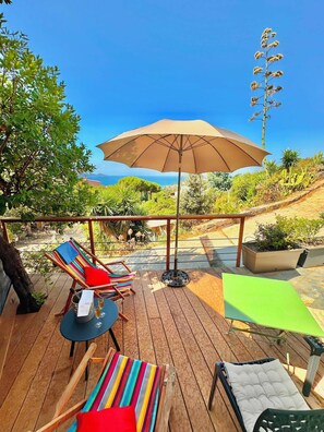 A wooden deck with outdoor seating, including a table and chairs, and a large umbrella providing shade. - One-bedroom apartment in Rupione with exceptional ocean views, a 6-minute walk from the beach (Pietrosella)