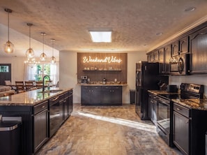 A modern kitchen with dark cabinetry, a central island, pendant lighting, and a neon sign reading 'Weekend Vibes'. - Weekend Vibes - 1 Level - Pool - Hot Tub - Fenced Yard (Sevierville)