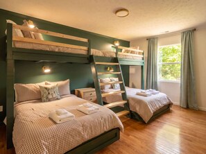 Quarto com beliches, uma escada, janela com cortinas e mesa de cabeceira com abajur.