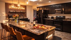 A modern kitchen with a large island, dark cabinetry, stainless steel appliances, and a neon sign. - Weekend Vibes - 1 Level - Pool - Hot Tub - Fenced Yard (Sevierville)