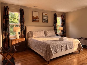 A bedroom with a bed, two bedside lamps, a nightstand, a wooden floor, and two wall-mounted paintings. - Weekend Vibes - 1 Level - Pool - Hot Tub - Fenced Yard (Sevierville)
