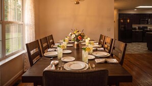 A dining room with a long table set for six, featuring a chandelier, floral centerpiece, and a view of the kitchen. - Weekend Vibes - 1 Level - Pool - Hot Tub - Fenced Yard (Sevierville)