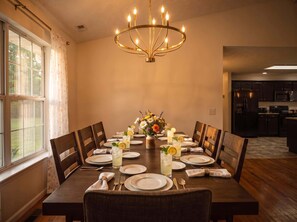 Uma sala de jantar com uma mesa comprida posta para seis pessoas, com um candelabro, arranjo floral e vista para a cozinha.