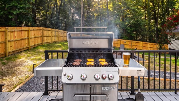 A barbecue grill with four burgers cooking, a beer glass, and a wooden deck. - Weekend Vibes - 1 Level - Pool - Hot Tub - Fenced Yard (Sevierville)