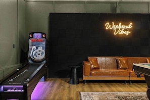 A billiards table, a neon sign, a brown leather sofa, and a patterned rug in a room with wooden flooring. - Weekend Vibes - 1 Level - Pool - Hot Tub - Fenced Yard (Sevierville)