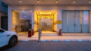 A hotel entrance with a glass facade, a car parked outside, and a fire hydrant on the sidewalk. - Zawaya Almasiya Alawali Apartments (Madinah)