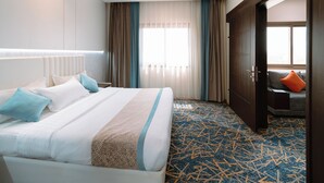 A hotel room with a large bed, a desk, and a view of the city through the window. - Zawaya Almasiya Alawali Apartments (Madinah)