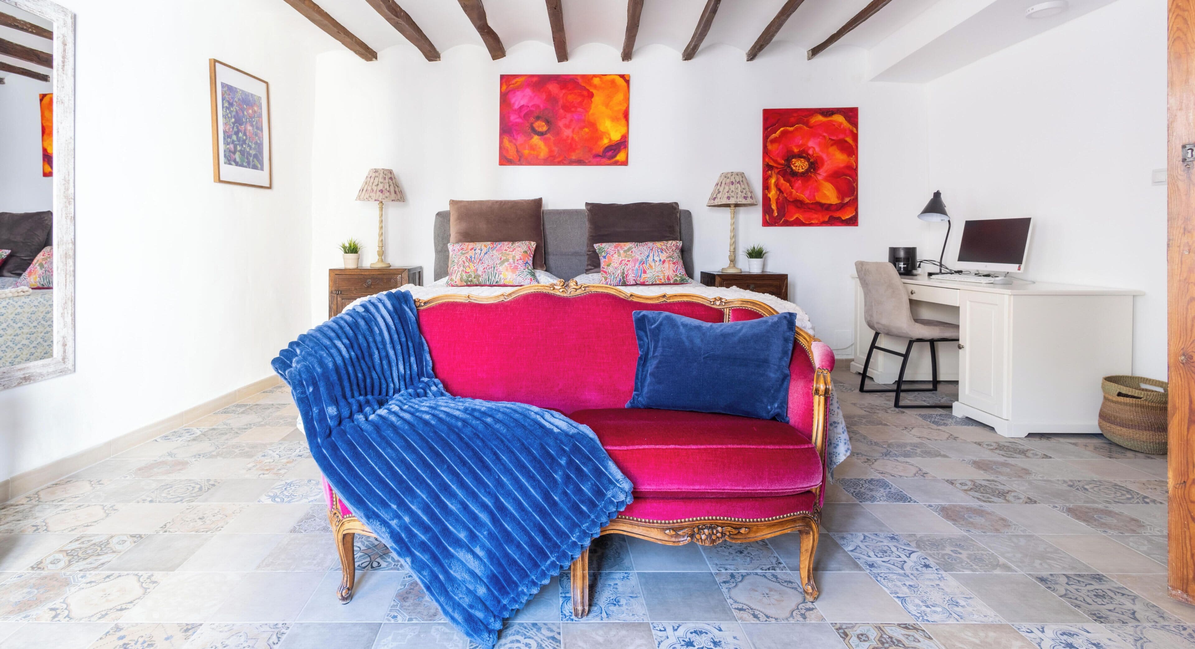 A room with a red velvet sofa, a blue throw, a wooden desk, and a computer.