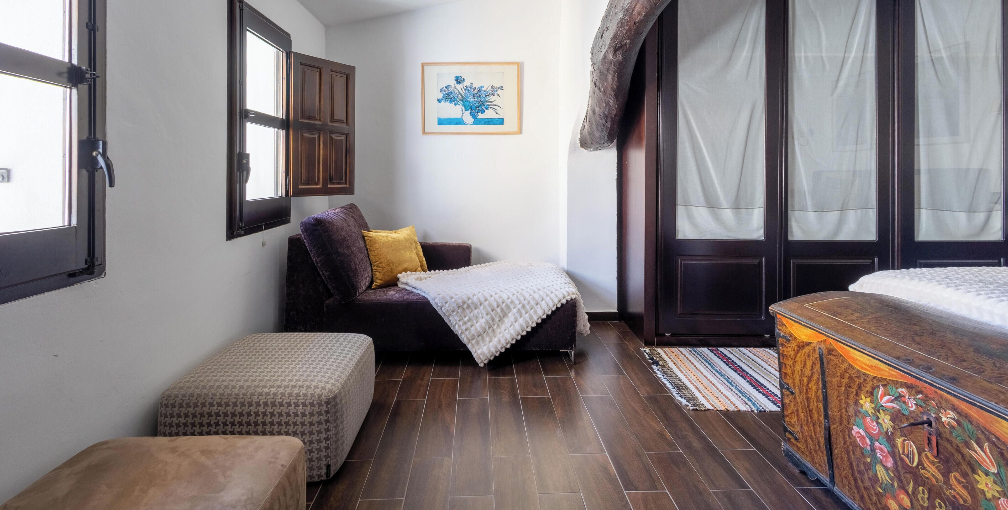 Una habitación compacta con cama, un pequeño sofá, un banco y un armario.