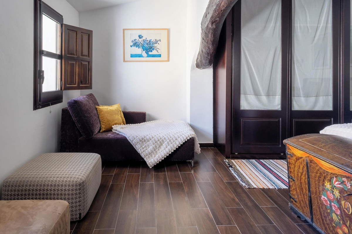 A compact room with a bed, a small sofa, a bench, and a cabinet.