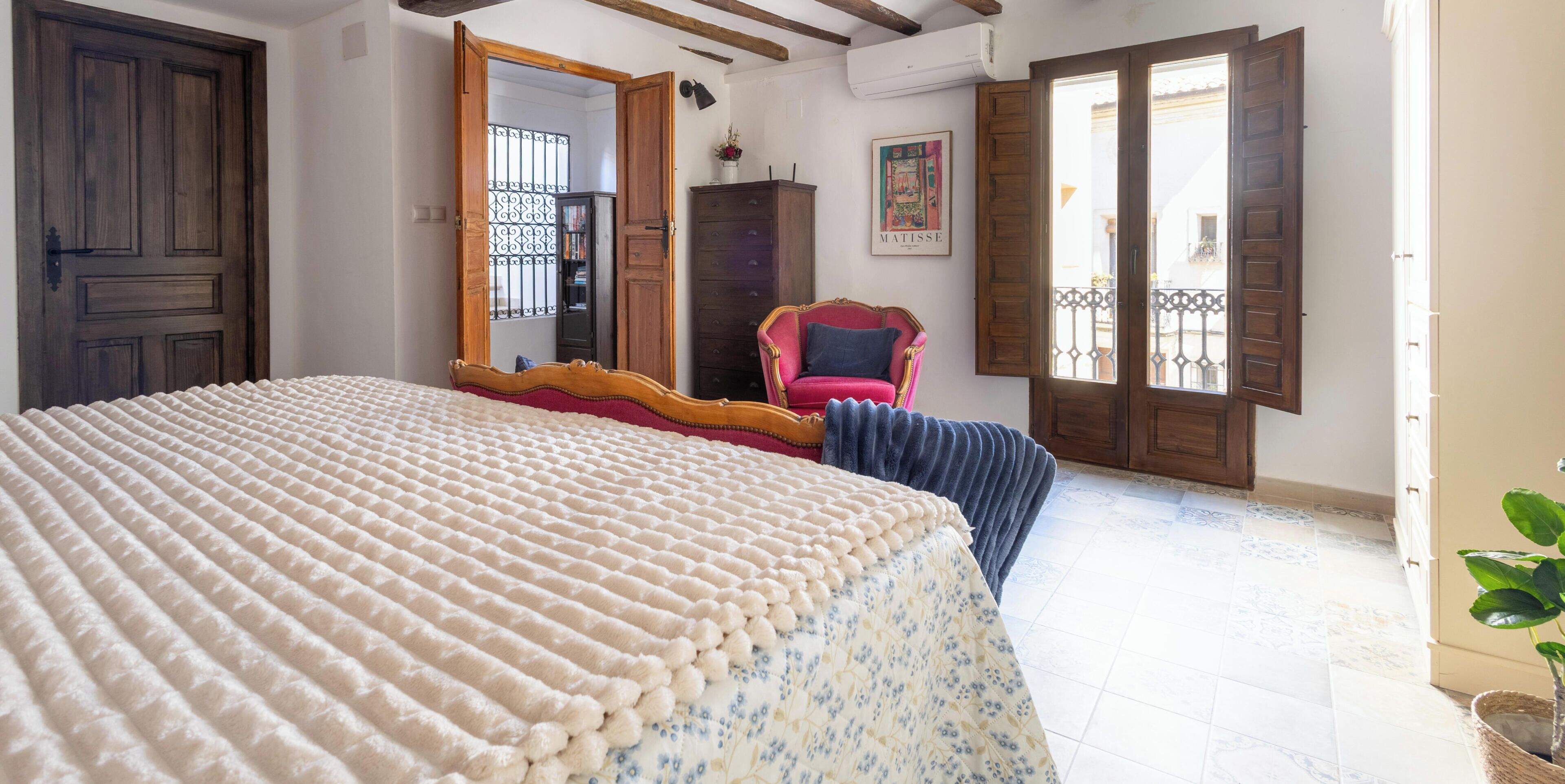 A bedroom with a bed, a chair, a wardrobe, and a door.