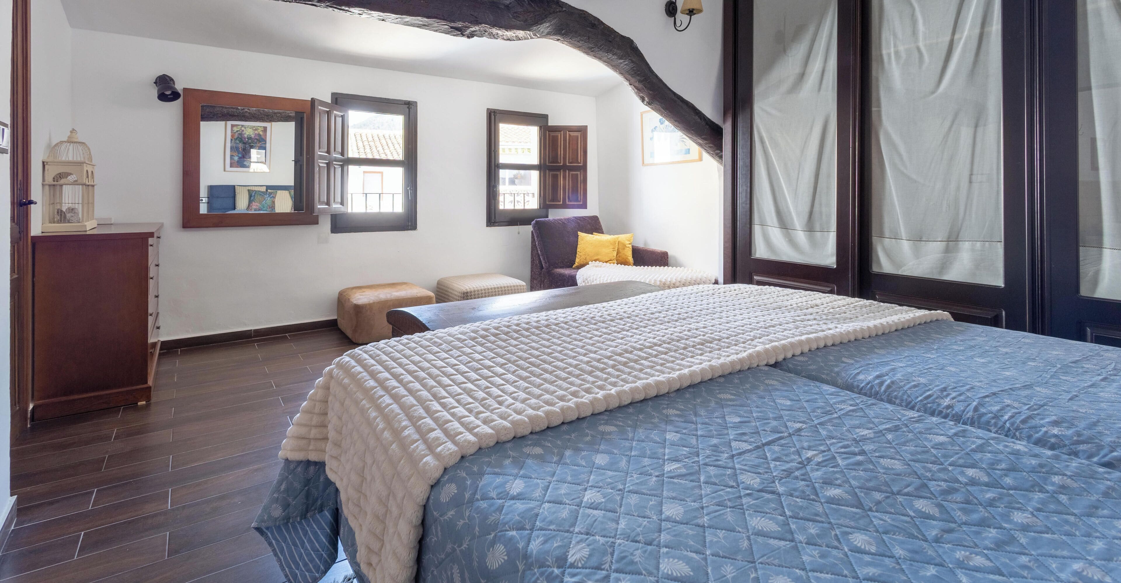 Un dormitorio con una cama grande, suelo de madera, una ventana con cortinas, una silla y una mesita de noche.