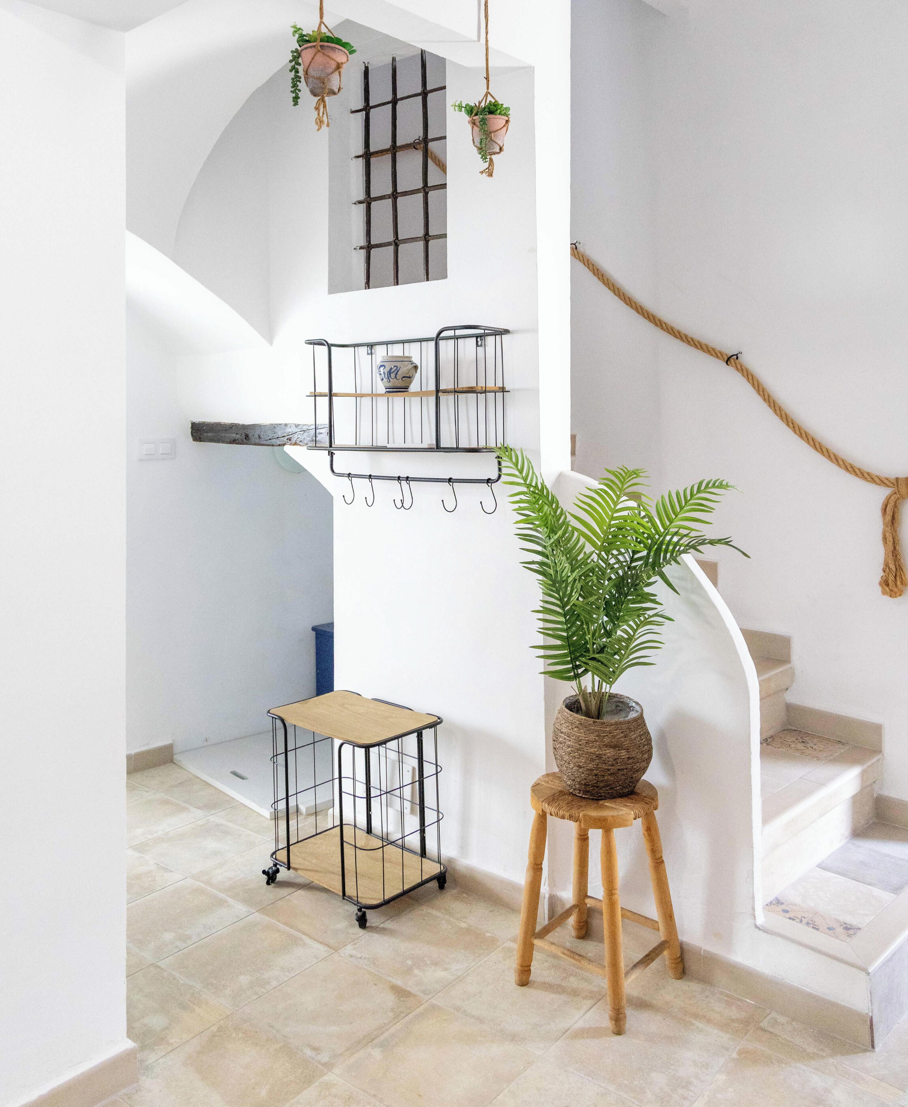 A staircase with a white wall, a metal shelf unit, a small wooden stool, and a potted plant.