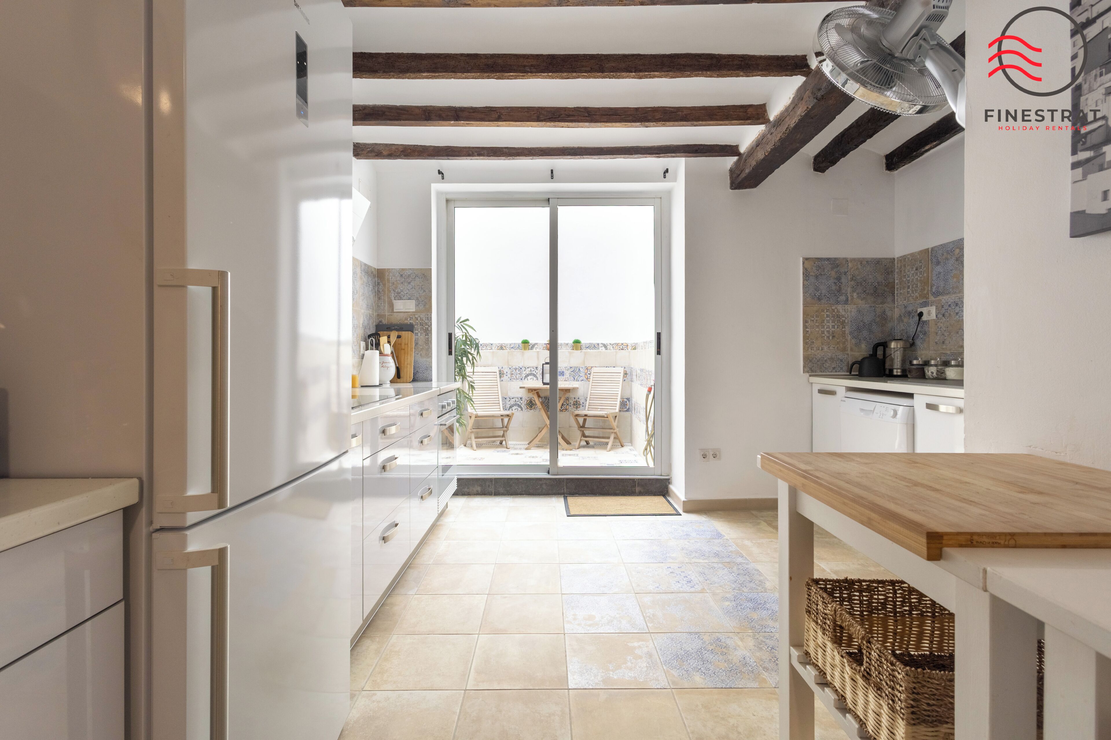 Une cuisine moderne dotée d’une porte-fenêtre coulissante donnant sur un balcon, un coin repas avec une table en bois et une vue sur la mer.