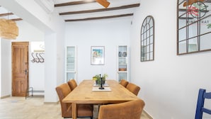 Un comedor con una mesa de madera y sillas tapizadas en tonos marrones, una pared blanca con un cuadro enmarcado, y una ventana con diseño de cuadrícula.