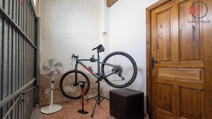 Una habitación con puerta de madera, una bicicleta apoyada en la pared, un ventilador y un pequeño altavoz negro.