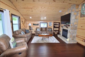 A cozy living room with leather sofas, a stone fireplace, and wooden walls. - Relax at Our Lake House Cottage-Heart of Osage Beach-One of a Kind (Osage Beach)